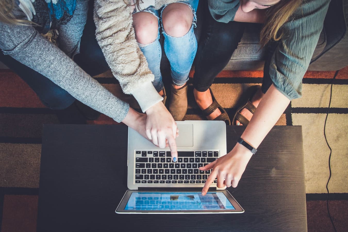three students sharing a laptop and using social media for education.