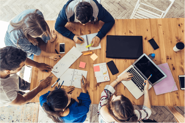 A group of students sit around a table and focus on finalizing a project from an online course.
