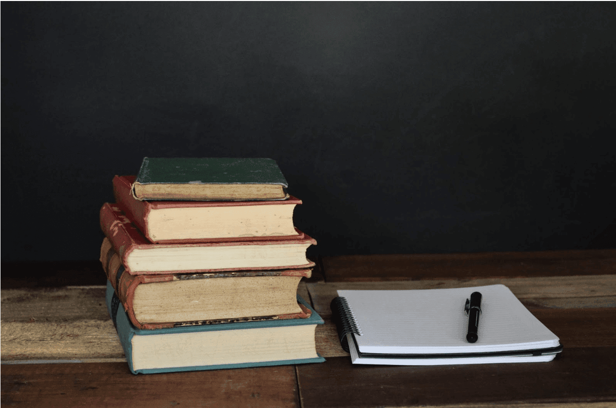 5 books stacked next to a notebook and pen that a student could use to write a literary analysis essay