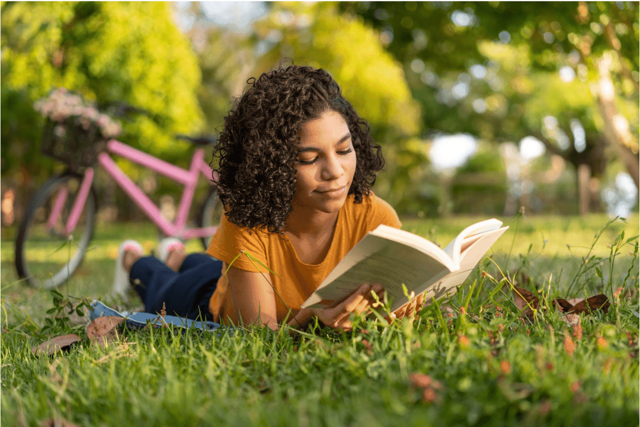A high school student takes a break from her bike ride to read in the park.